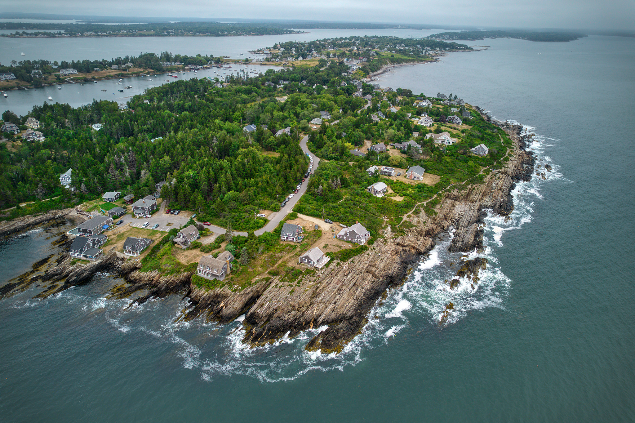 High-altitude aerial drone view of Bailey Island, Maine, featuring rocky shorelines, lush green forests, and coastal homes surrounded by the Atlantic Ocean.