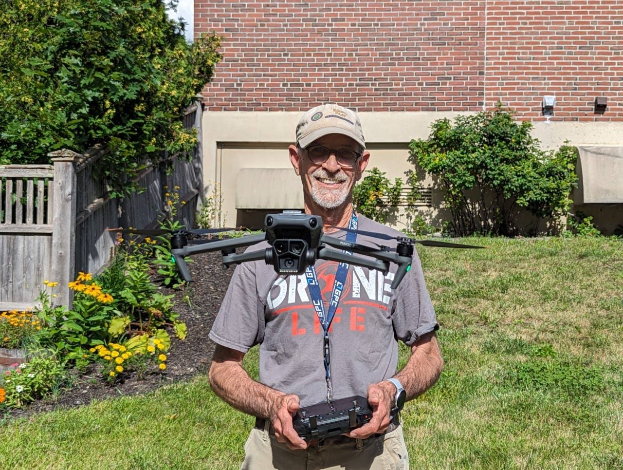 Mark smiling in a backyard holding a remote controller with a large, professional grade camera drone hovering safely in front of him.